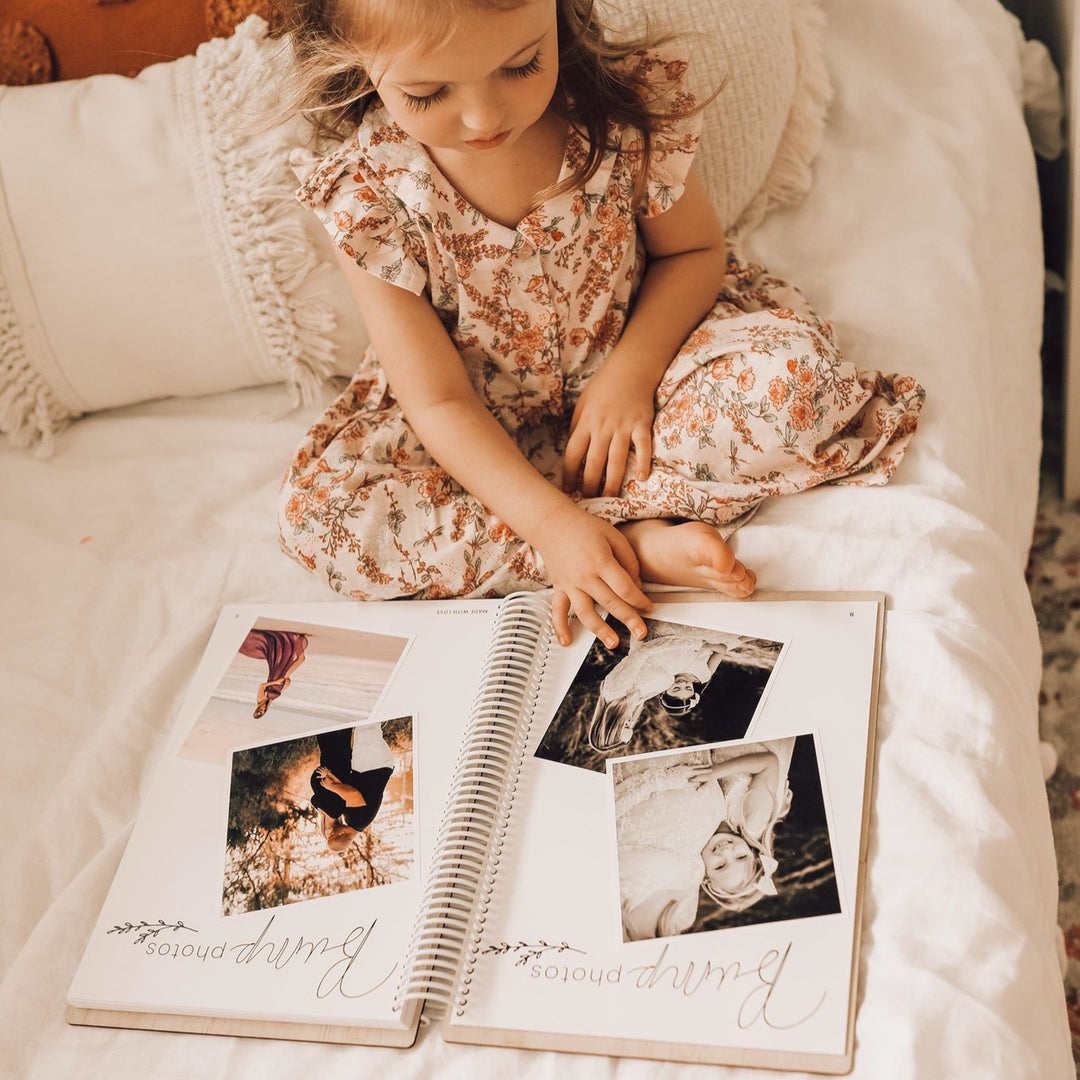 Young girl looking through Hello Fern wooden baby memory book of pregnancy photos on the 'Bump photos' pages.
