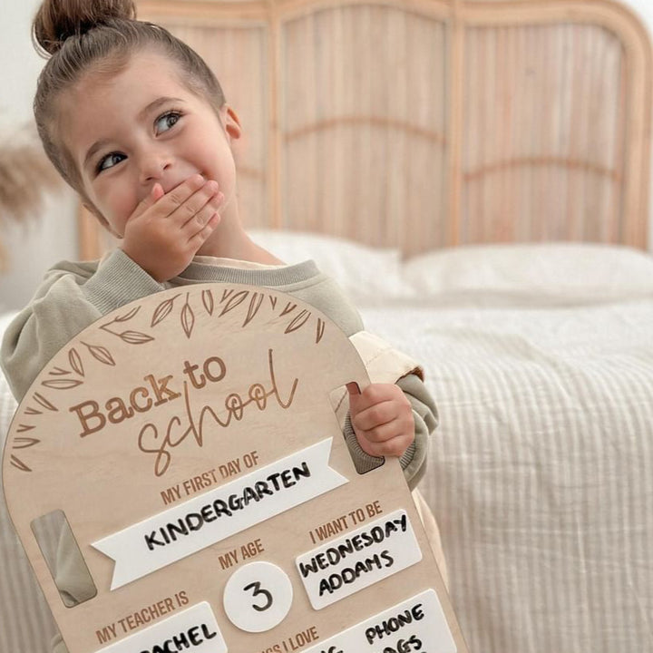 Kindergarten-aged little girl holding Hello Fern non-custom Back to School board covering her mouth with cute, cheeky expression.