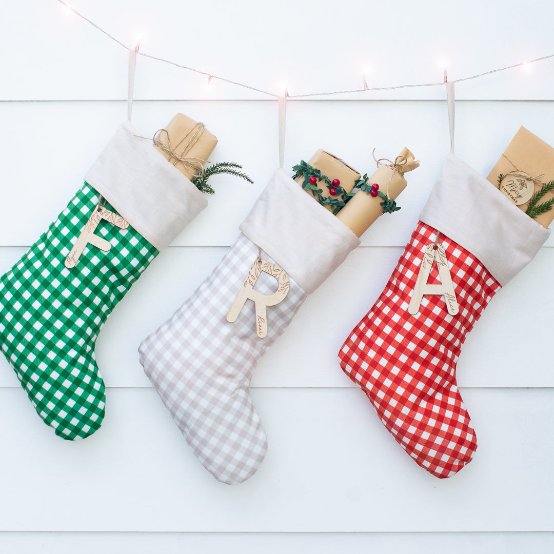 Set of three gingham Christmas stockings in green, brown, and red with custom wooden letter name plaques