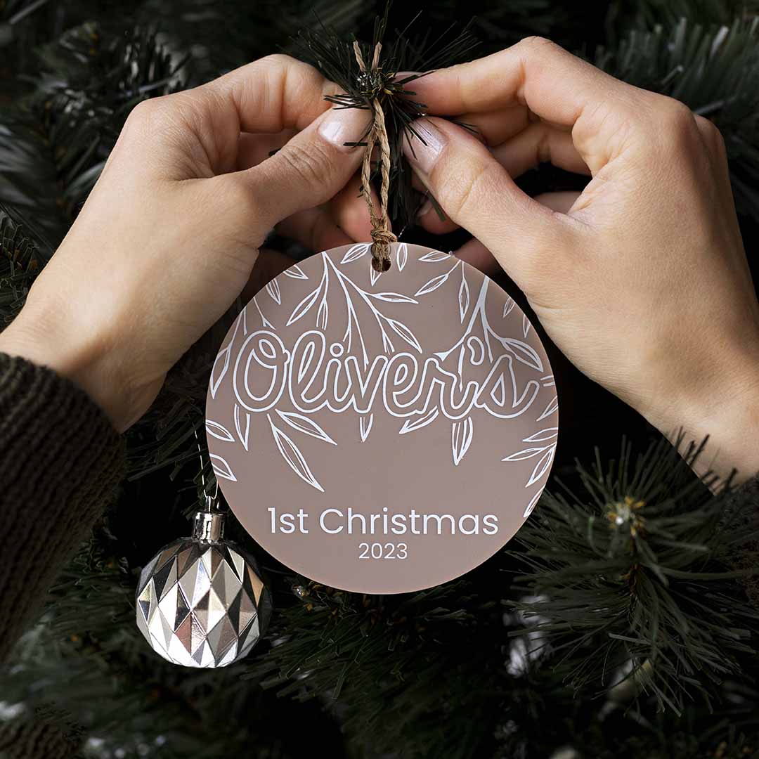 Hands hanging customisable Hello Fern acrylic 1st Christmas ornament on Christmas tree.