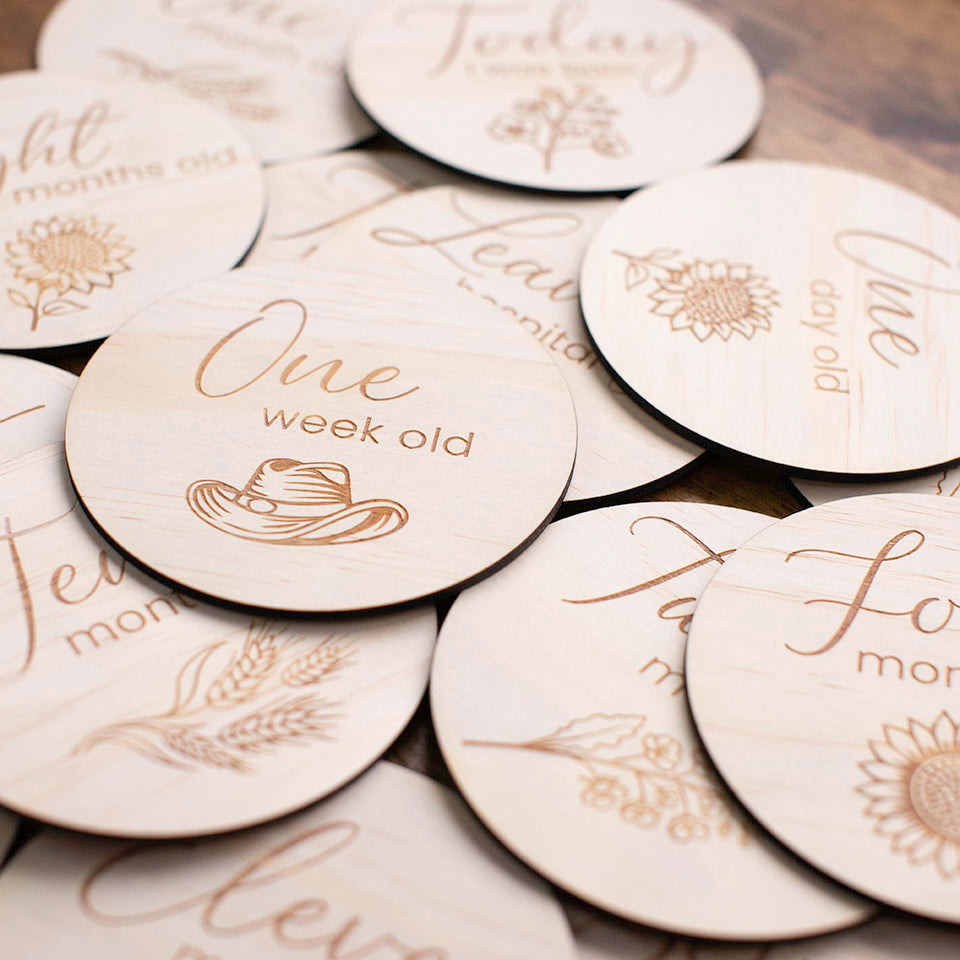 Closeup view of pile of wooden discs from the Hello Fern Country Month Milestone disc set featuring discs from baby's birth to twelve months old.