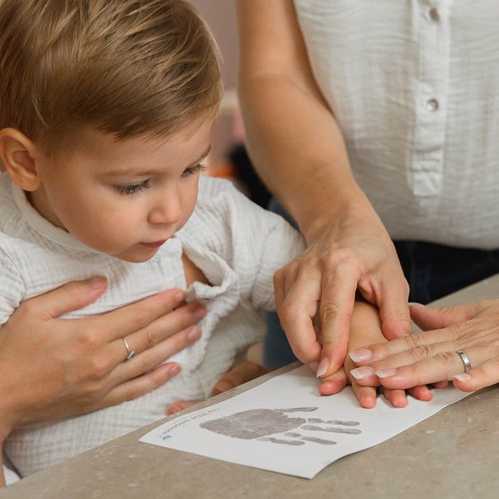 Mum pressing child's hand down to make hand prints on inkless print kit paper.