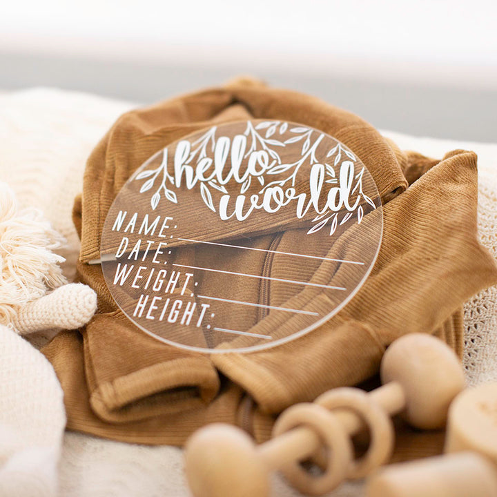 Closeup of Hello Fern clear acrylic 'Hello Word' plaque with white wording on baby clothes.