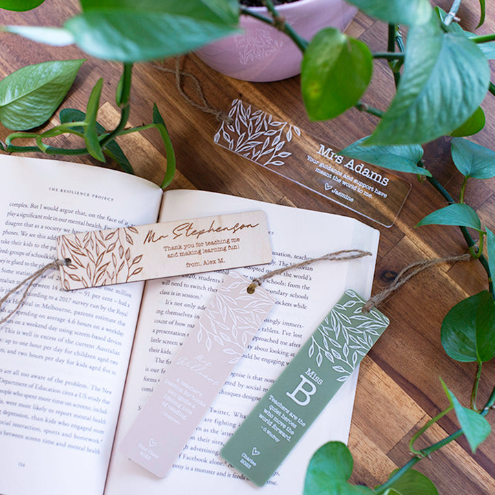 Custom Hello Fern teacher bookmarks top view on book with plant including both wooden and acrylic options.