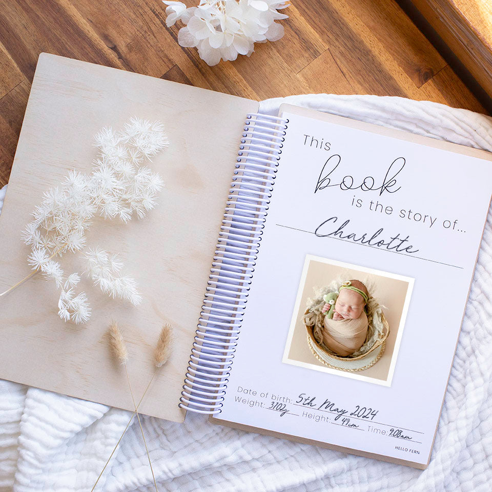 Flat lay showing inside front cover of non-custom same-sex Hello Fern wooden baby memory book with photo and birth details of baby.