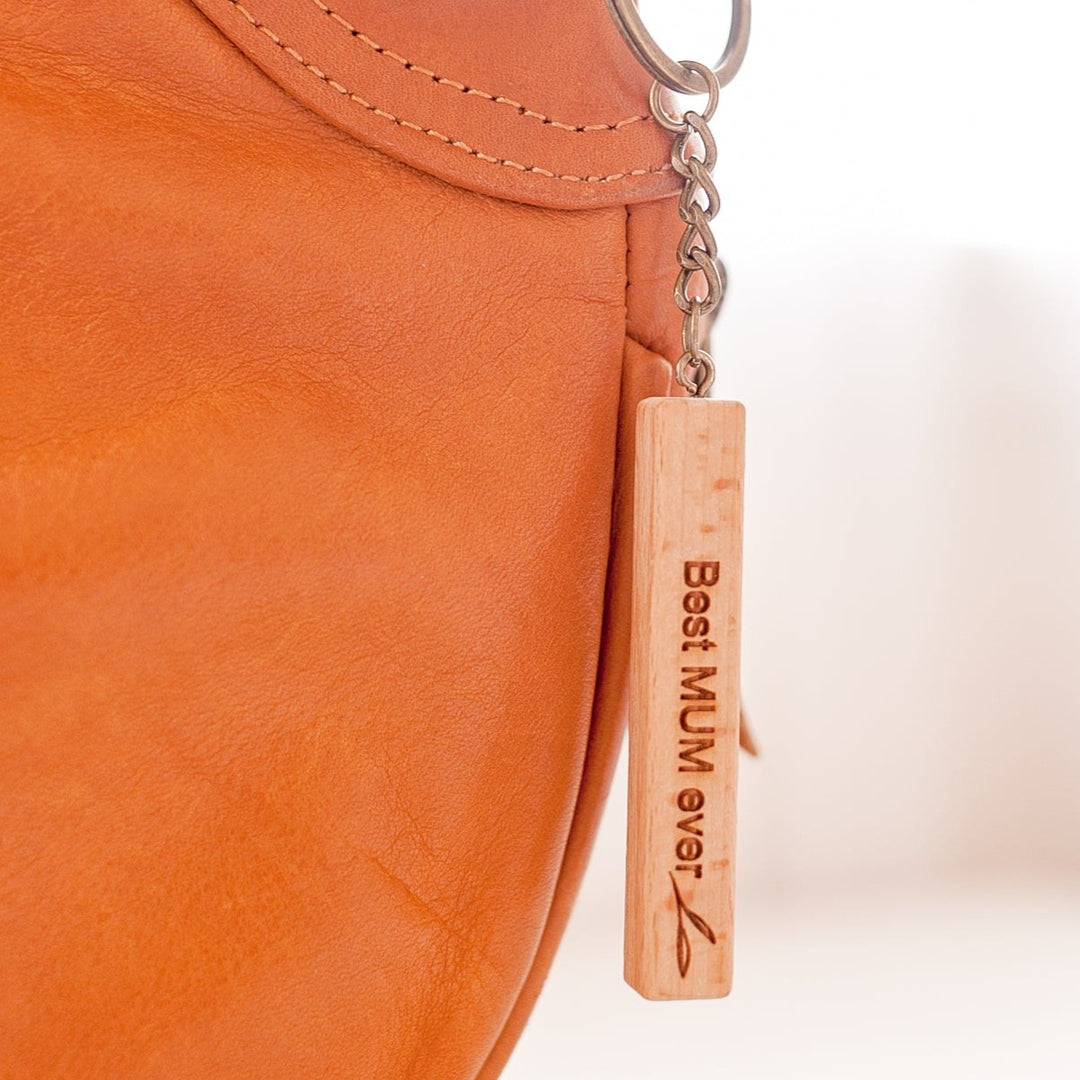 Closeup of Hello Fern light wooden Mother's Day keyring hanging from brown leather bag.