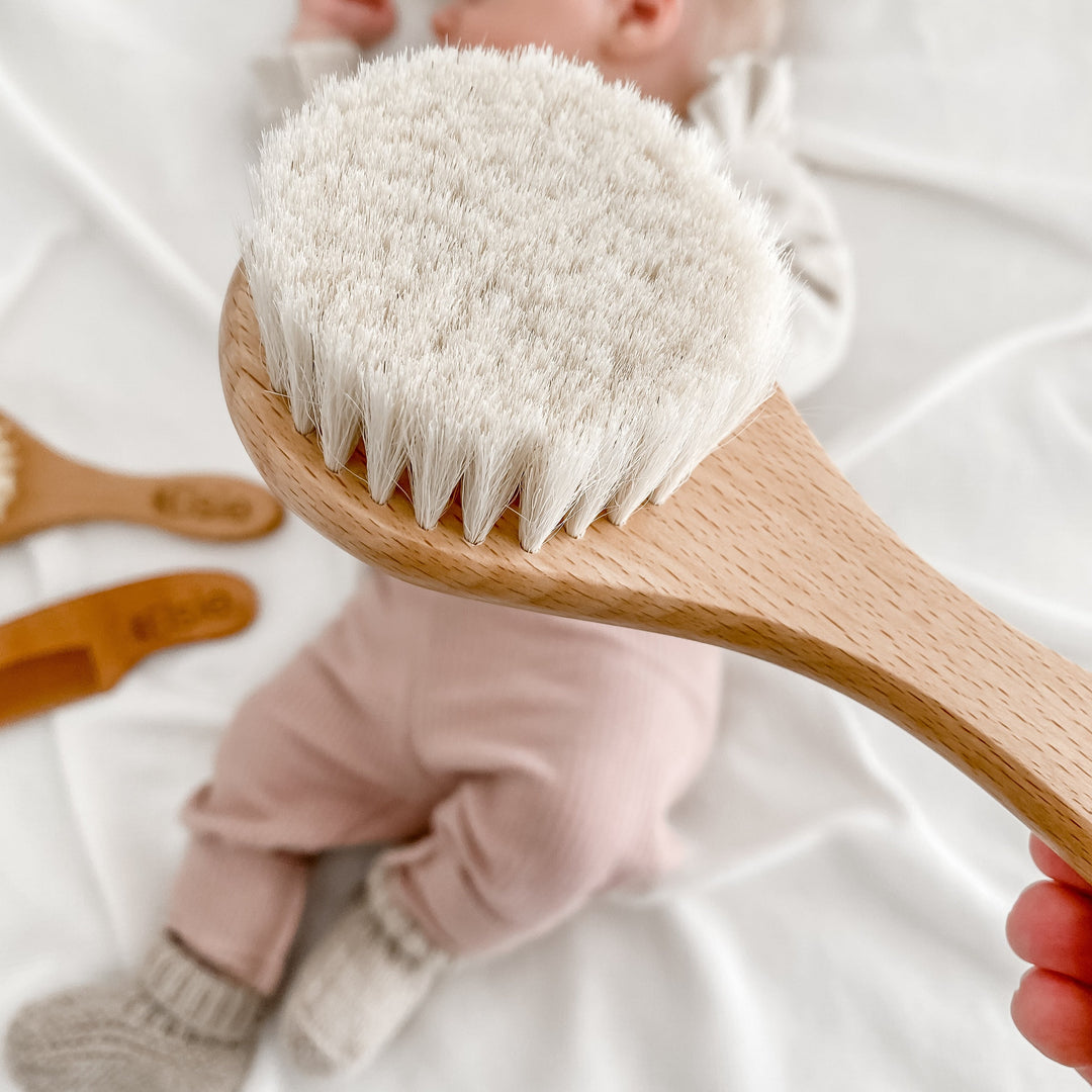 Closeup of Hello Fern's soft goat's hair baby brush with newborn lying on bed in the background.