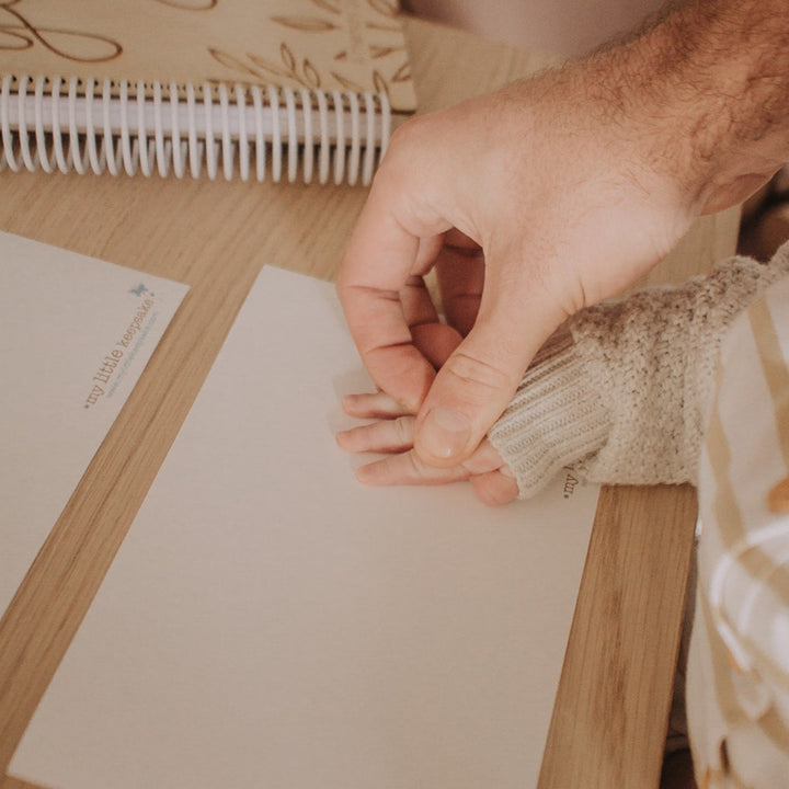 Dad pressing child's hand down to make hand print on inkless print kit paper.