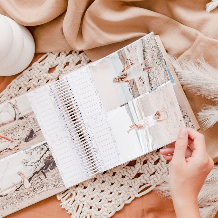 Top view of the inside of a Hello Fern wooden photo album showing photos, spaces for captions, and a hand turning the page.