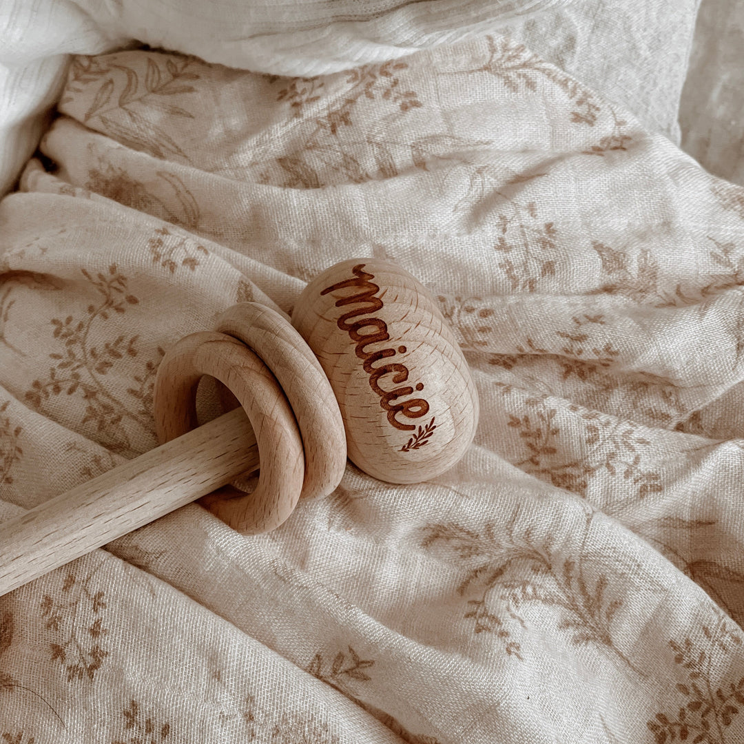 Closeup of wooden baby rattle with name Maicie etched in to rattle.