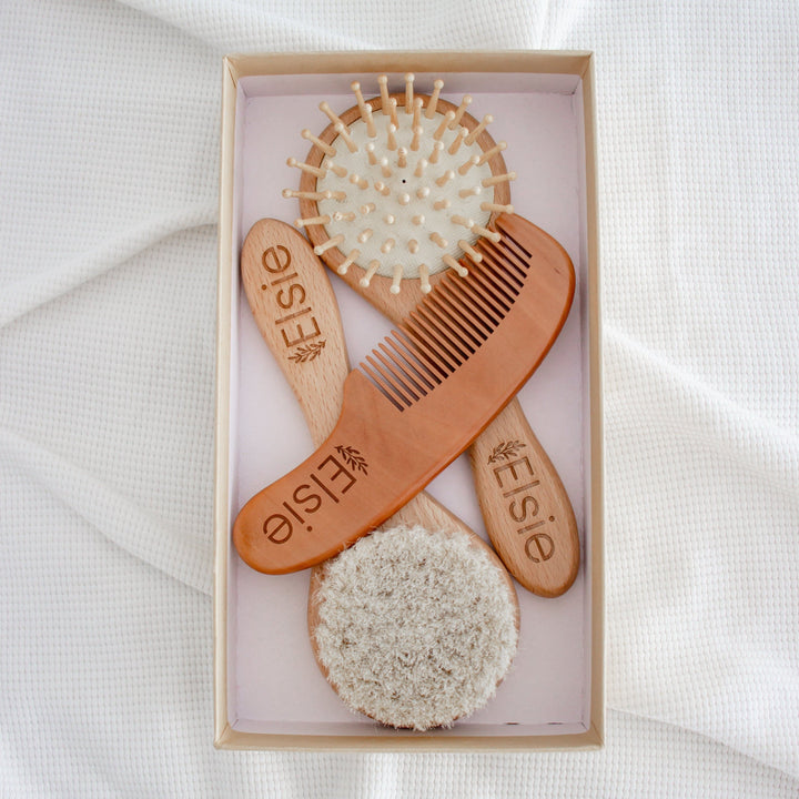 Flatlay showing the three brush options of the custom Hello Fern baby brush set including a massage brush, a soft goat's hair brush, and a comb with baby's name etched onto the wooden handles.