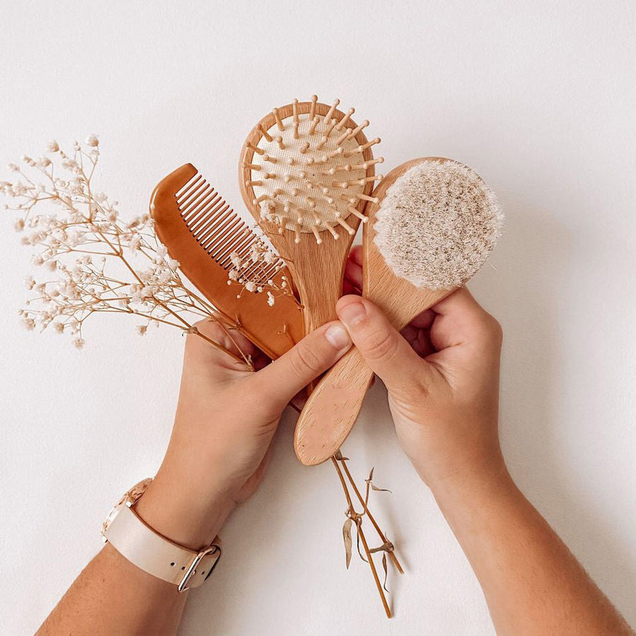 Hands holding a Hello Fern non-custom brush set including two wooden baby brushes and a comb