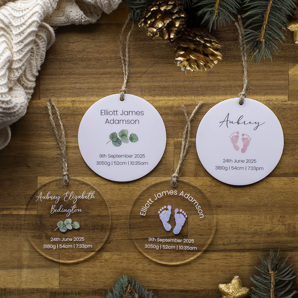 Four Hello Fern personalised acrylic baby Christmas ornament discs custom printed with birth details on a wooden surface with decorative elements.