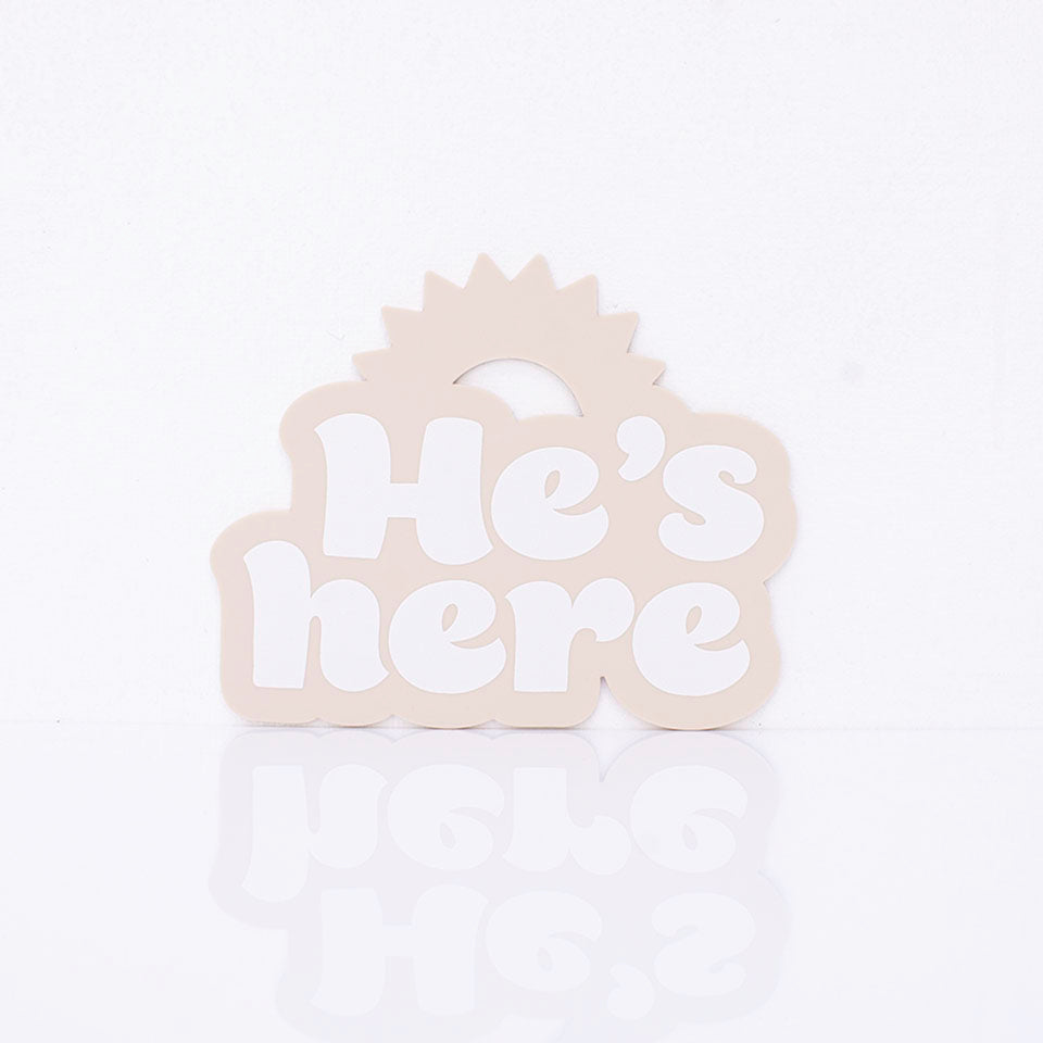 Hello Fern beige acrylic birth announcement shaped with a rising sun silhouette and around printed words "He's here".