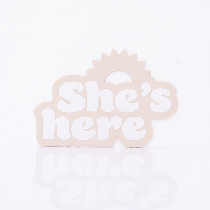 Hello Fern beige acrylic birth announcement shaped with a rising sun silhouette and around printed words "She's here".