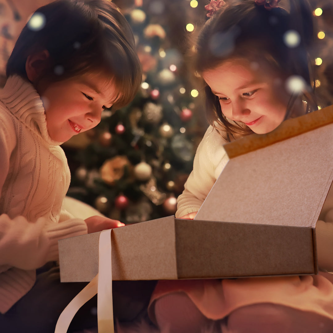 Boy and girl with smiles on faces  in front of Christmas tree opening Christmas Eve box.