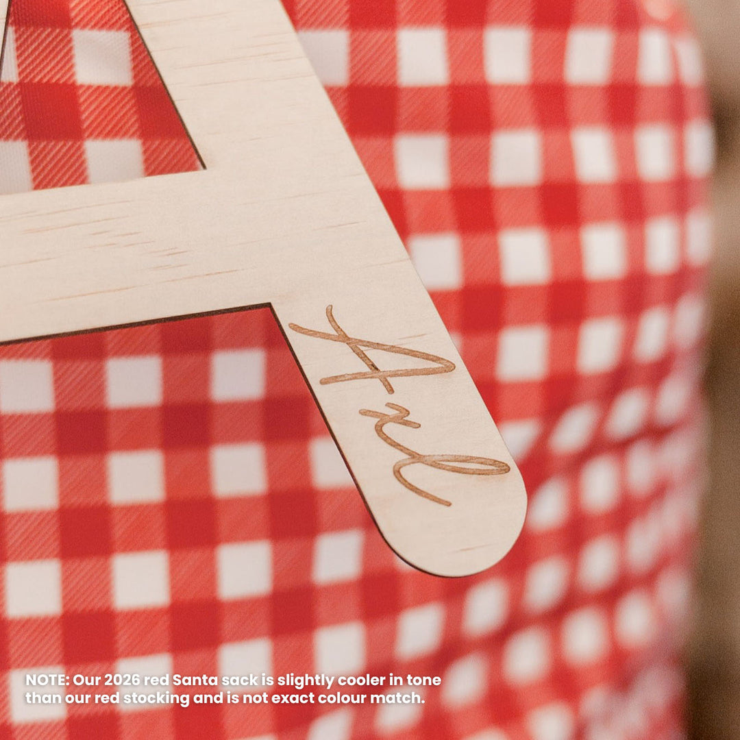 Closeup of red Christmas Santa sack with wooden letter 'A' plaque and name 'Axl' etched into plaque.