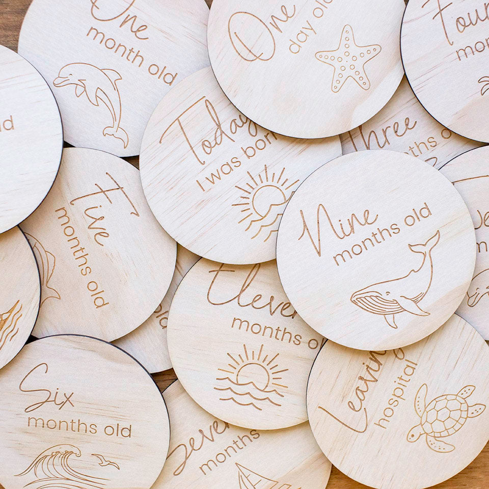 Close up of Hello Fern wooden baby achievement ocean-themed milestone discs with engraved text and illustrations for baby's first year.