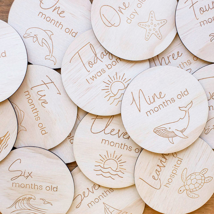 Close up of Hello Fern wooden baby achievement ocean-themed milestone discs with engraved text and illustrations for baby's first year.