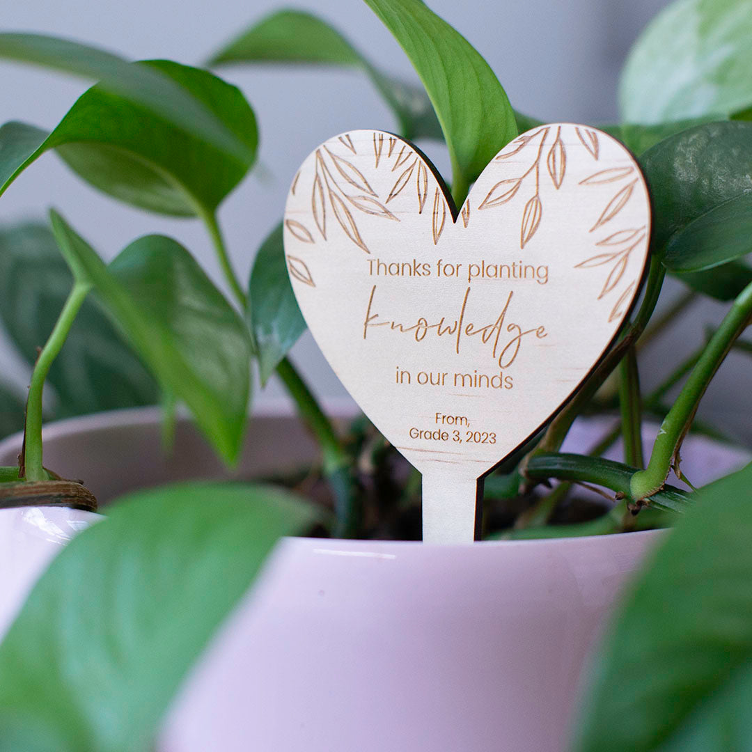 Teacher gift wooden heart-shaped plant stake with 'Thank you for helping me grow' message and custom sign-off shown in potted plant.