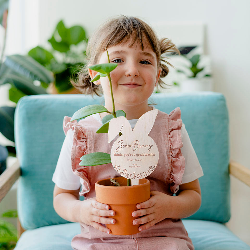 Cute girl holding potted plant with hello fern wooden Easter plant stake gift for teacher.