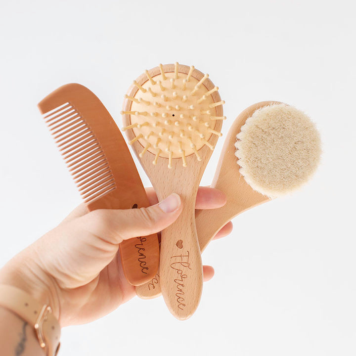 Set of custom etched wooden baby brushes including a comb and two brushes held by a hand on a light background.