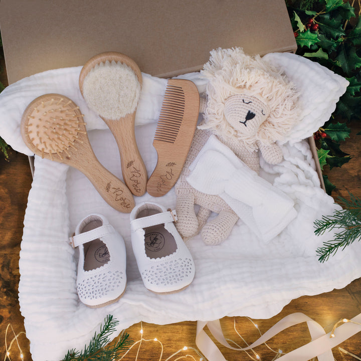 View of gifts inside Christmas Eve box including custom baby hair brushes, lion plushie, baby bow, and baby booties.