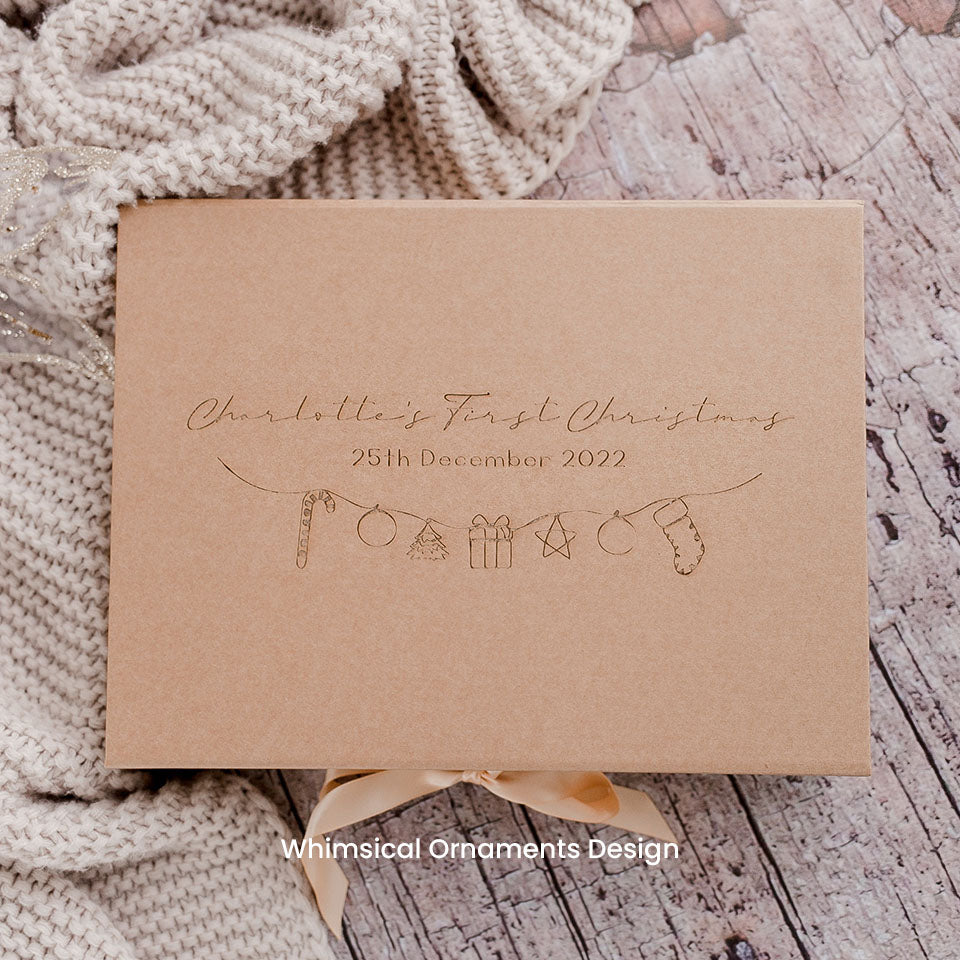 Hello Fern kraft paper custom keepsake Christmas Eve gift box in whimsical ornaments design with the words 'Charlotte's First Christmas' etched on lid and festive illustrations on a textured surface.