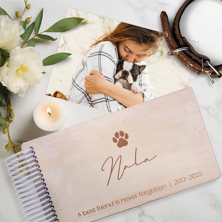 Flatlay of Hello Fern custom mini wooden photo album gift with a pet memorial theme including woman hugging dog, dog collar, candle, and flowers.