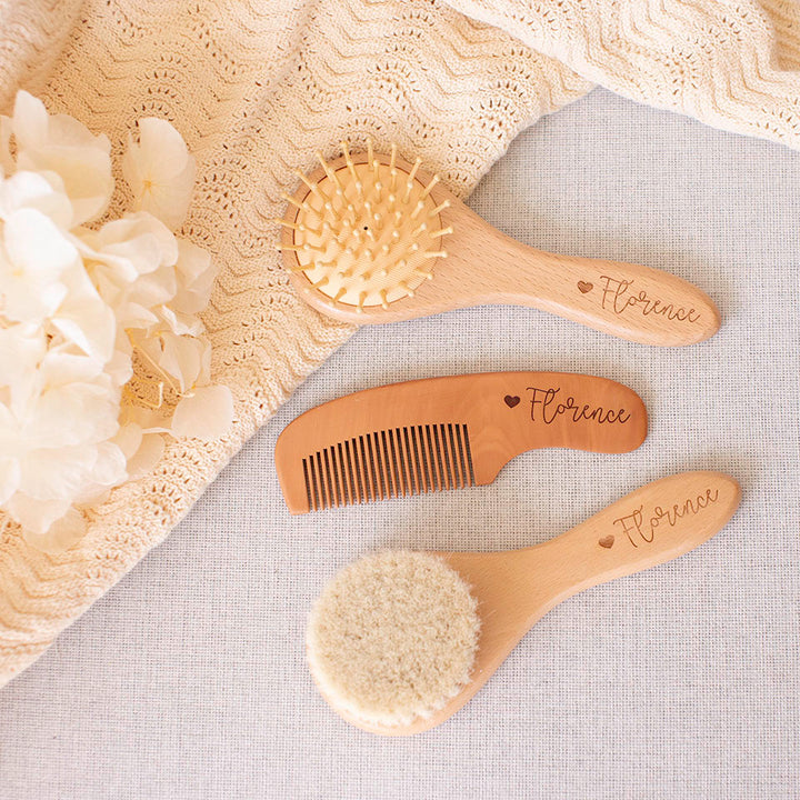 Set of wooden baby brushes and comb custom etched with 'Florence' and heart on a soft, textured fabric background.