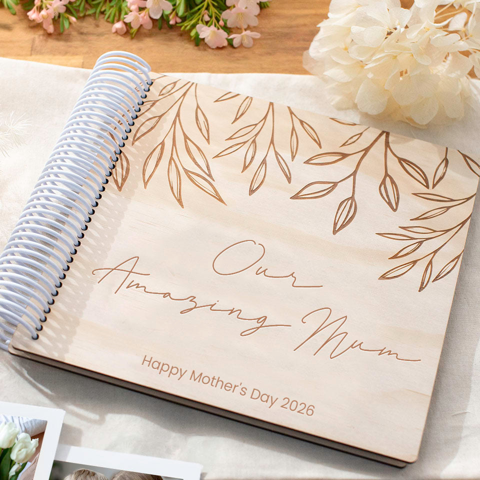 Personalised Hello Fern wooden Mother's Day photo album with 'Our Amazing Mum' and 'Happy Mother's Day 2026' on a wooden surface with flowers.