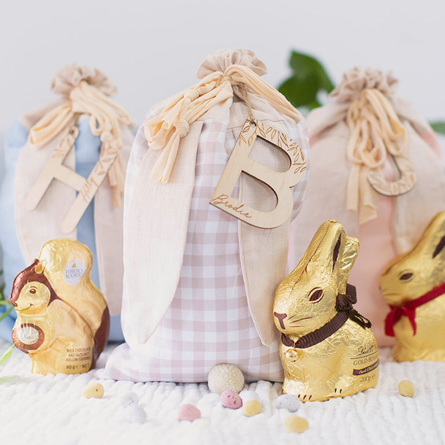 Hello Fern Easter Sacks with custom wooden letter name plaque sitting on table with chocolate bunnies and eggs.