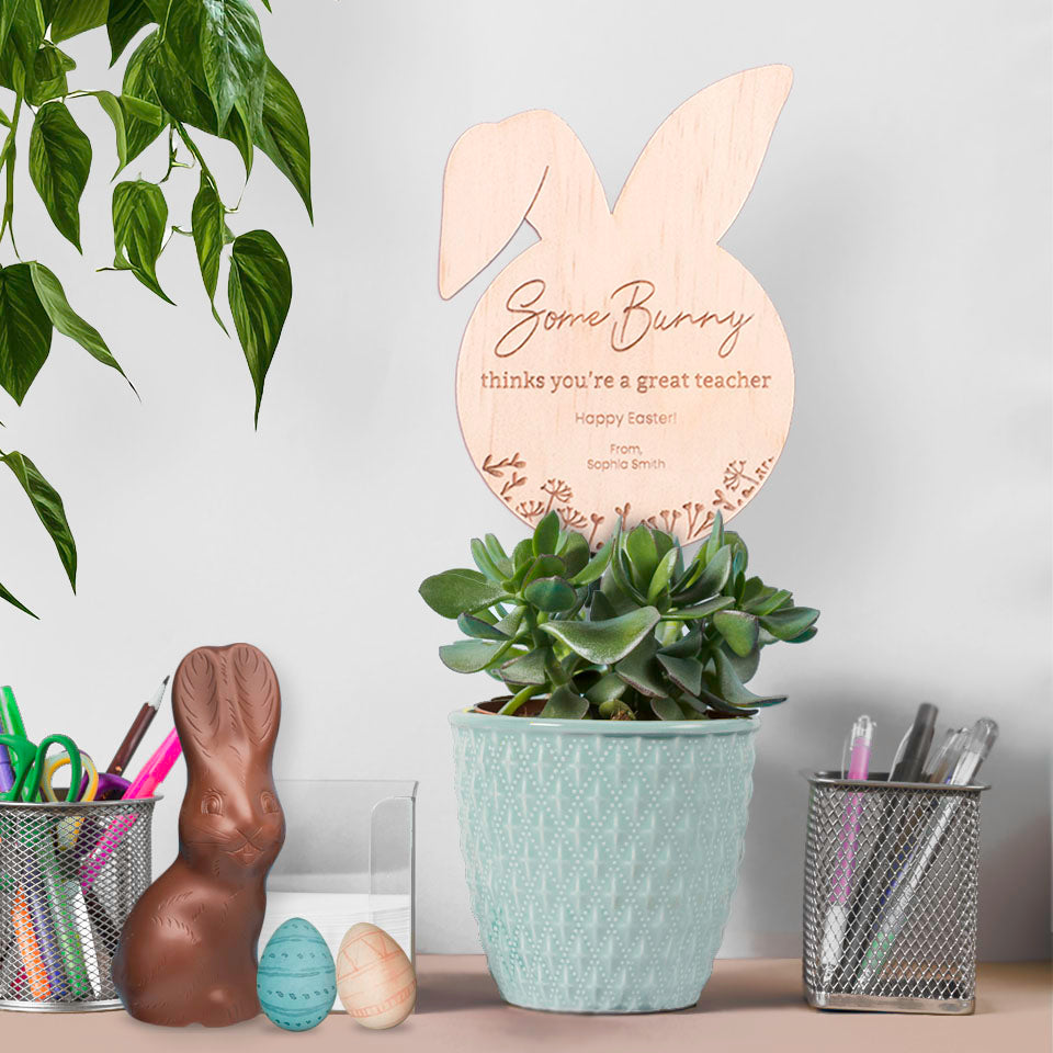 Hello Fern custom wooden Easter plant stake in plant pot on teacher's desk with stationery and easter egg chocolate.