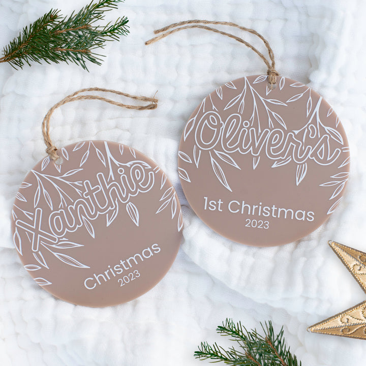 Flatlay with pine needles showing two acrylic Christmas ornaments with customisable child's name and year.