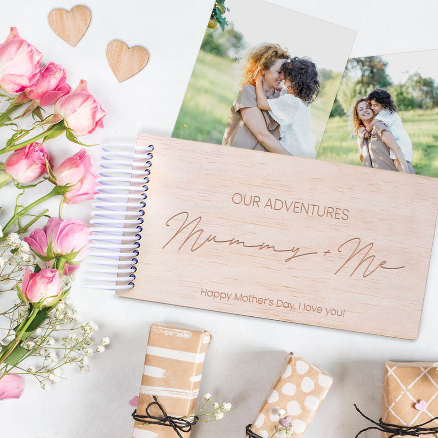Personalised Hello Fern Mother's Day wooden photo album titled 'Our Adventures Mummy + Me' with flowers and gift boxes on a white background