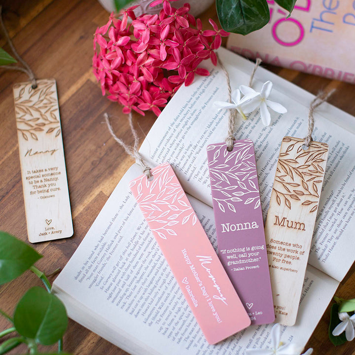 Top view of wooden and acrylic Hello Fern Mother's Day custom bookmarks on book with flowers. 