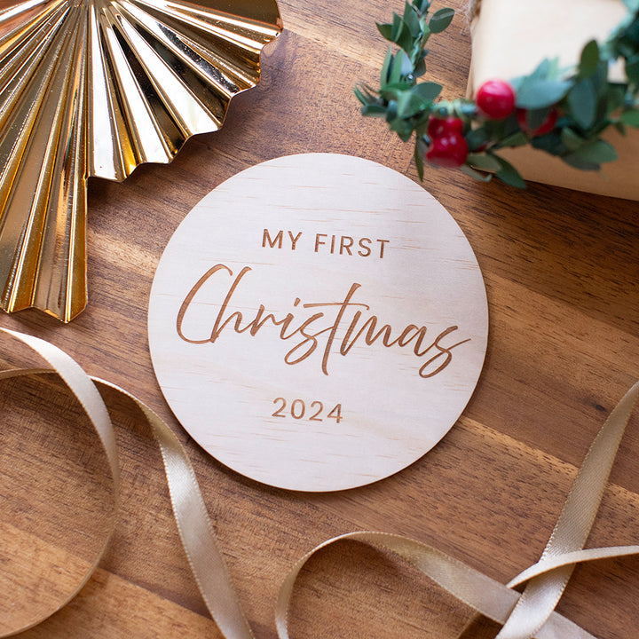 Hello Fern non-custom timber "My first Christmas" disc flat lay with ornament, present, holly, and ribbon.