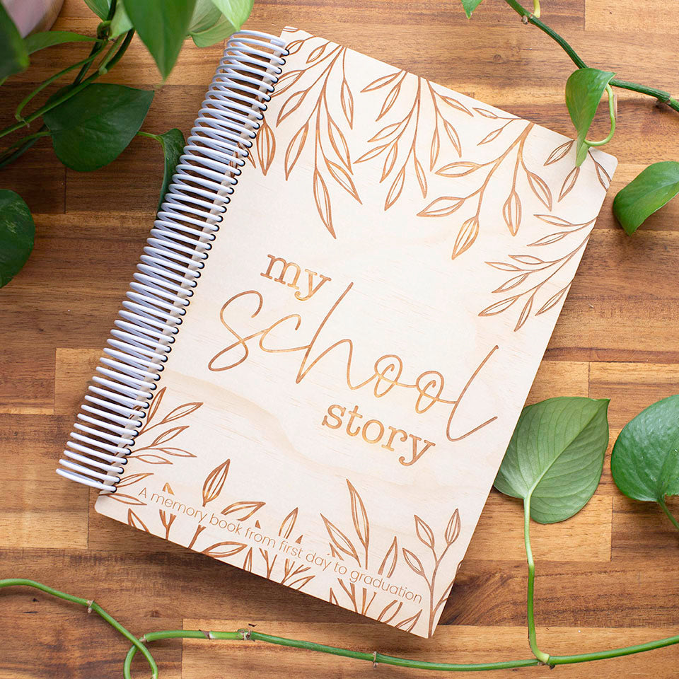 Top view of Hello Fern non-custom "My School Story" wooden school years book on wooden table with vines surrounding.