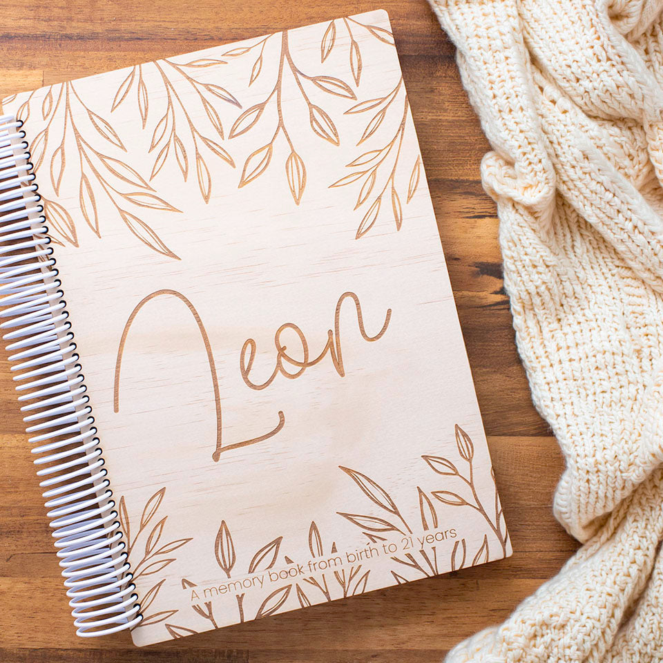 Hello Fern personalised wooden baby book etched with name 'Leon' on a wooden surface with a knitted blanket