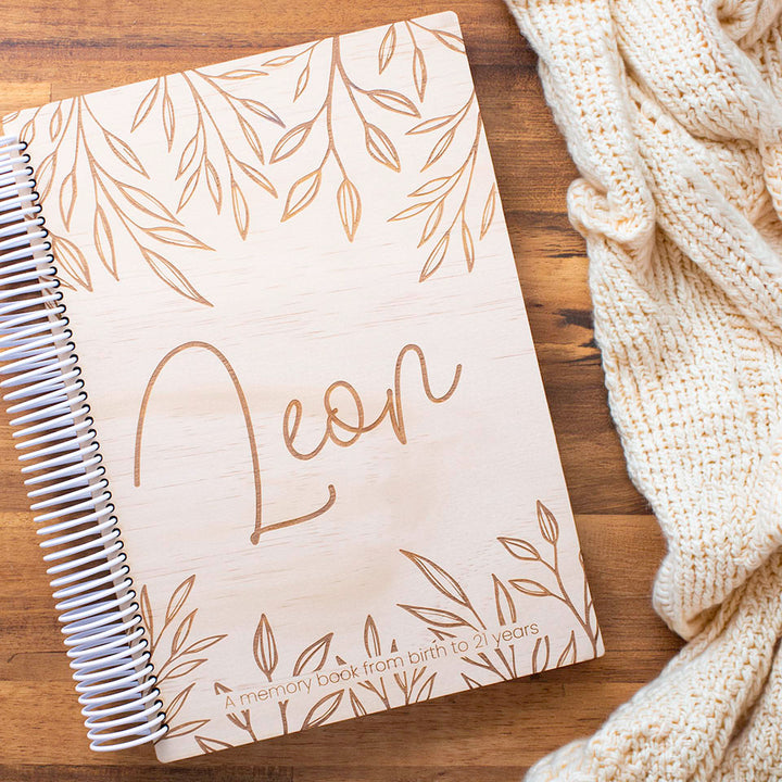 Hello Fern personalised wooden baby book etched with name 'Leon' on a wooden surface with a knitted blanket