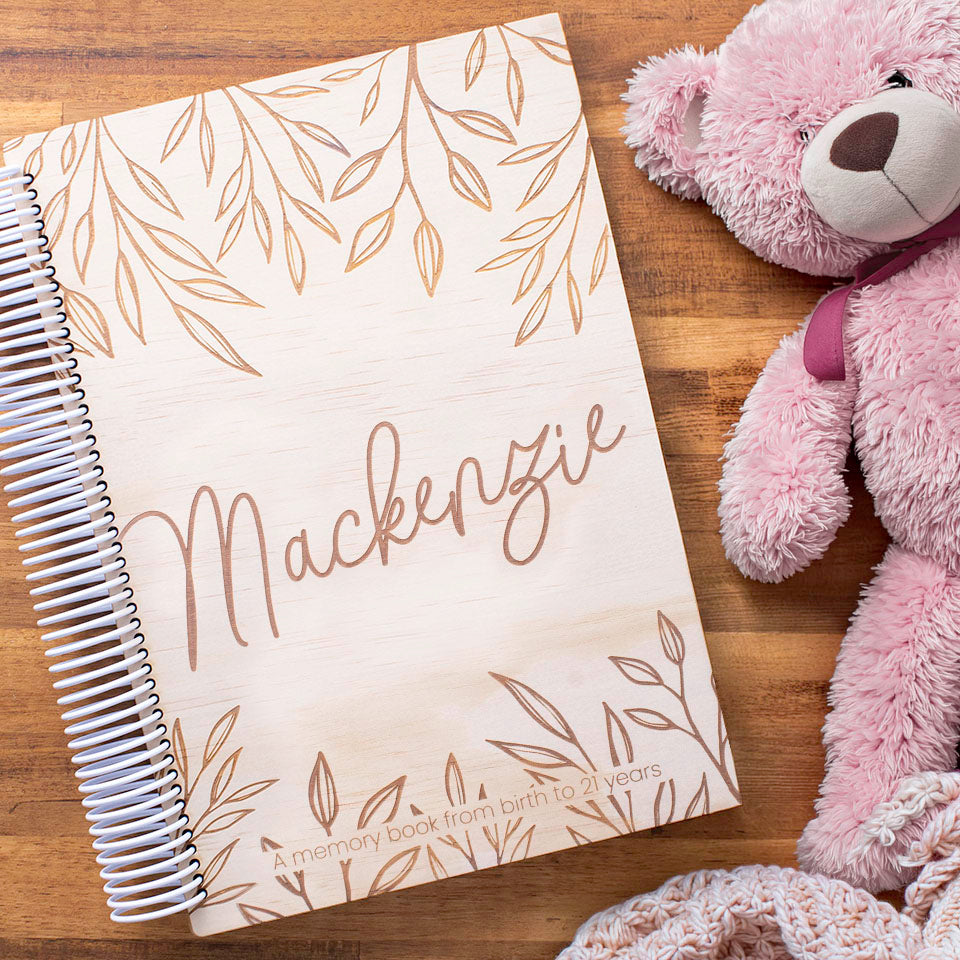 Hello Fern personalised wooden baby book etched with name 'Mackenzie' on a wooden surface with a pink teddy bear.