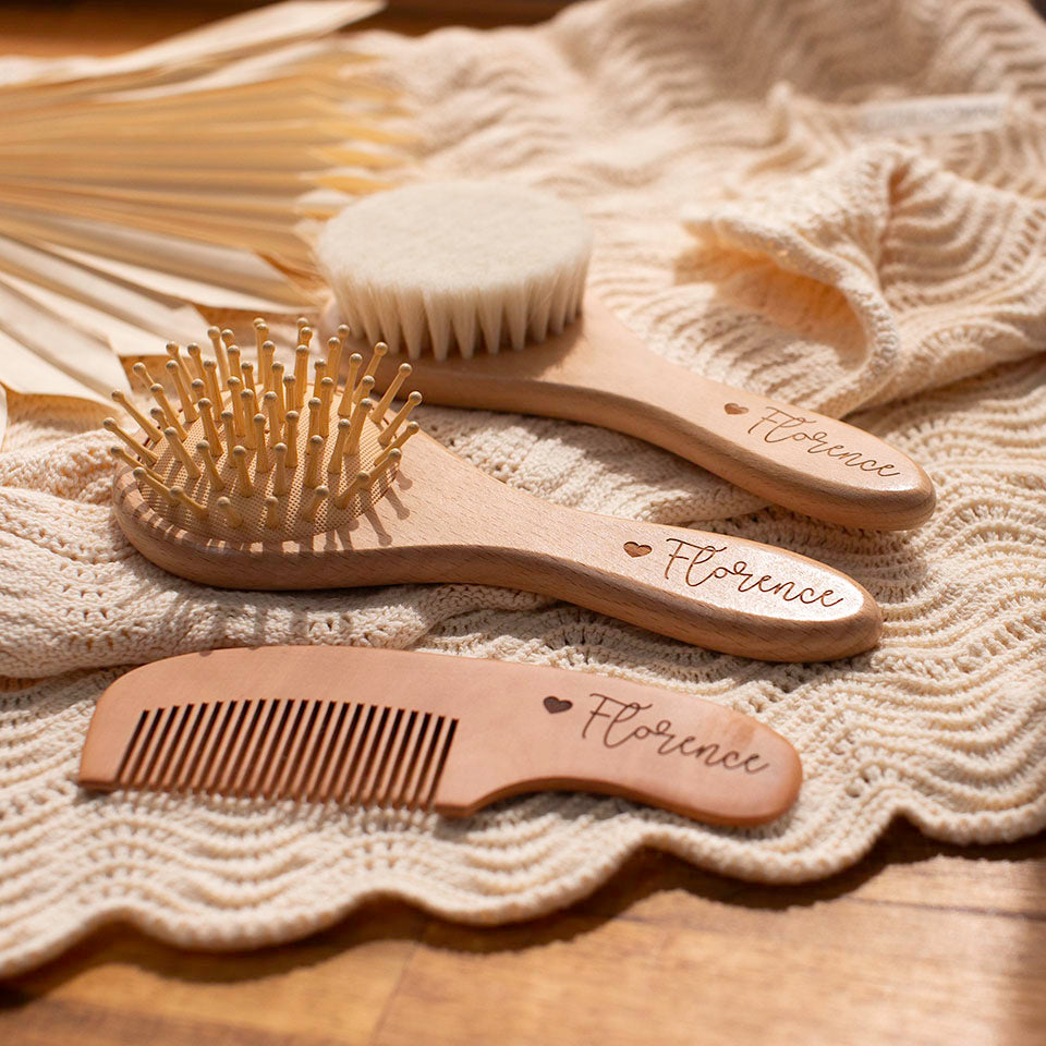 Personalised wooden baby hairbrush and comb set with 'Florence' engraving on a textured fabric background and natural lighting