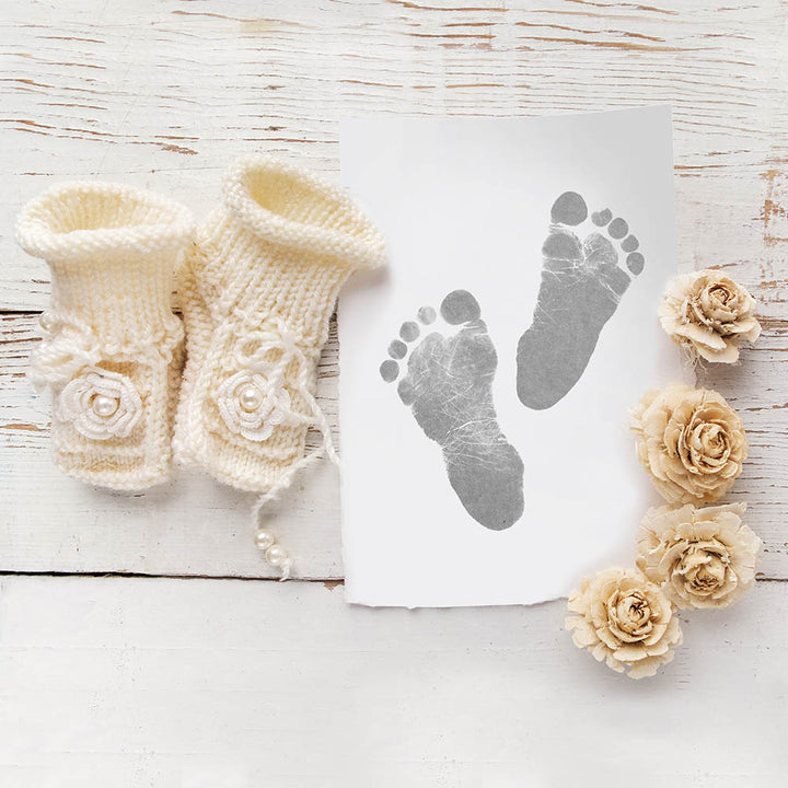 Baby's foot prints on flat lay with baby booties and flowers on wooden floor background.