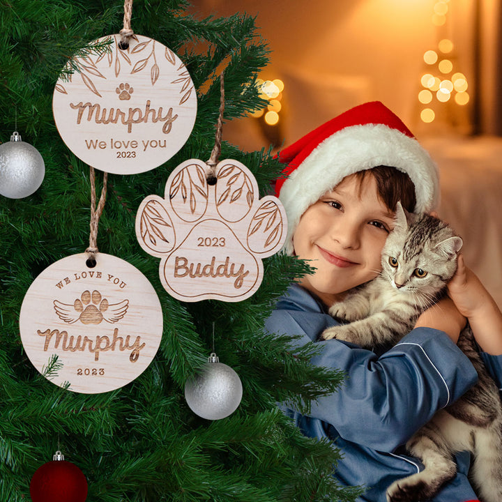 Little boy with Santa hat cuddling kitten beside Christmas tree featuring custom wooden Hello Fern pet ornaments.