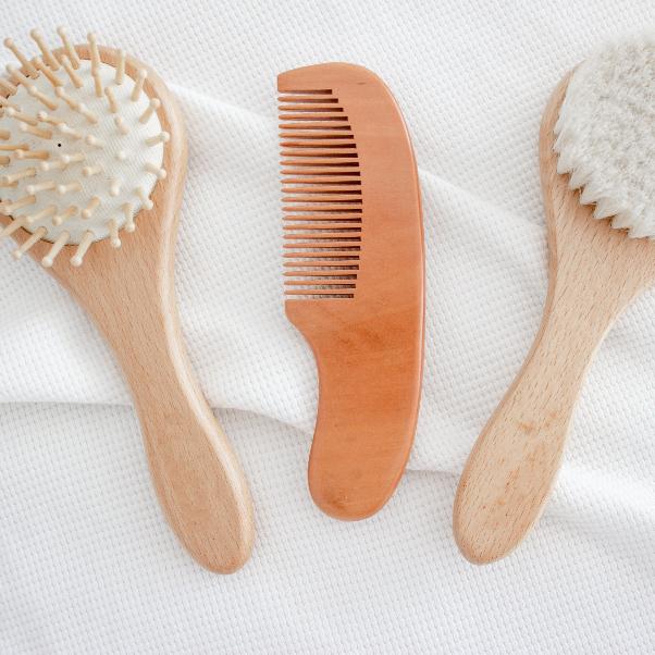 Flat lay showing each of the three brushes in the Hello Fern non-custom baby brush set including a massage brush, a comb, and a soft goat's hair brush.