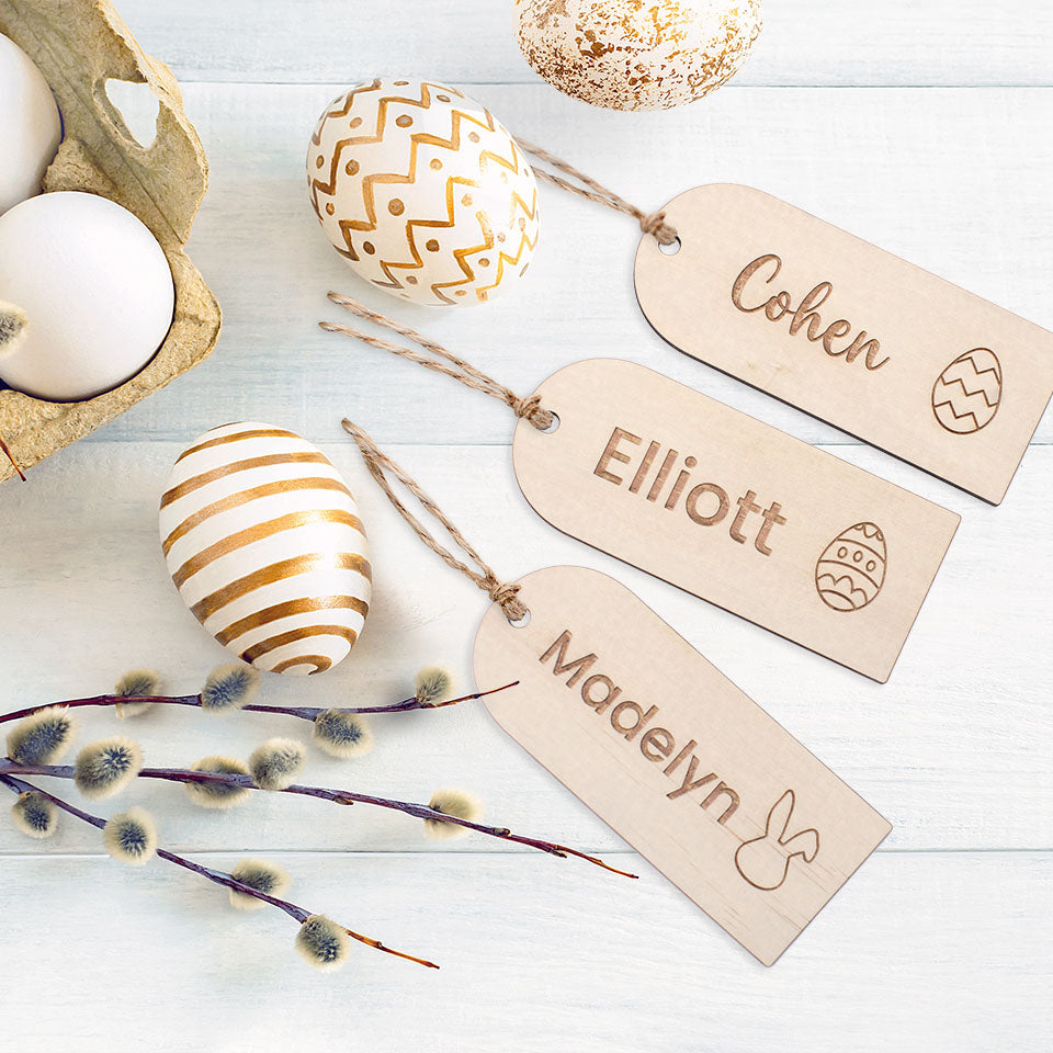 Flatlay image of three Hello Fern timber Easter basket tags customised with names on a table with golden painted Easter eggs.