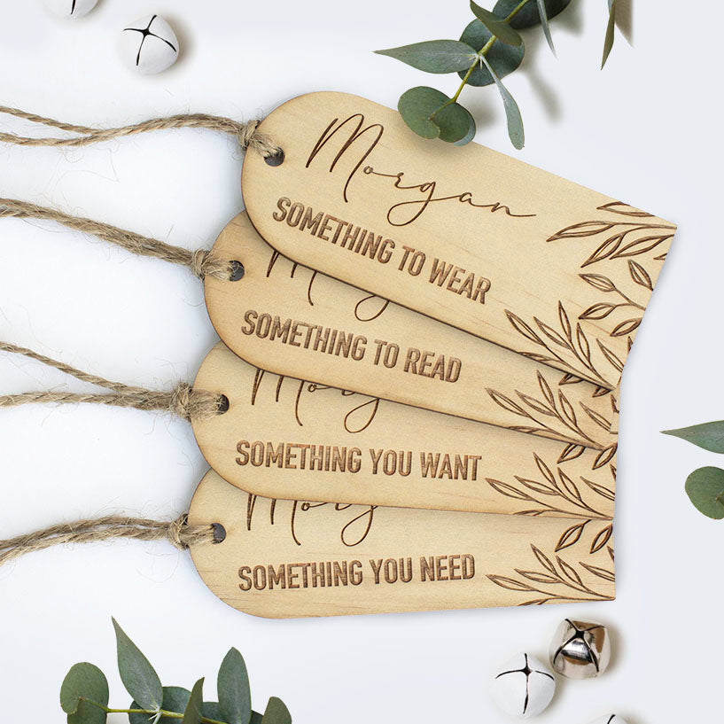 Top view of Hello Fern mindful gifting gift tags including 'something to wear', 'something to read', 'something you want', and 'something you need' with Christmas bells and leaves surrounding.