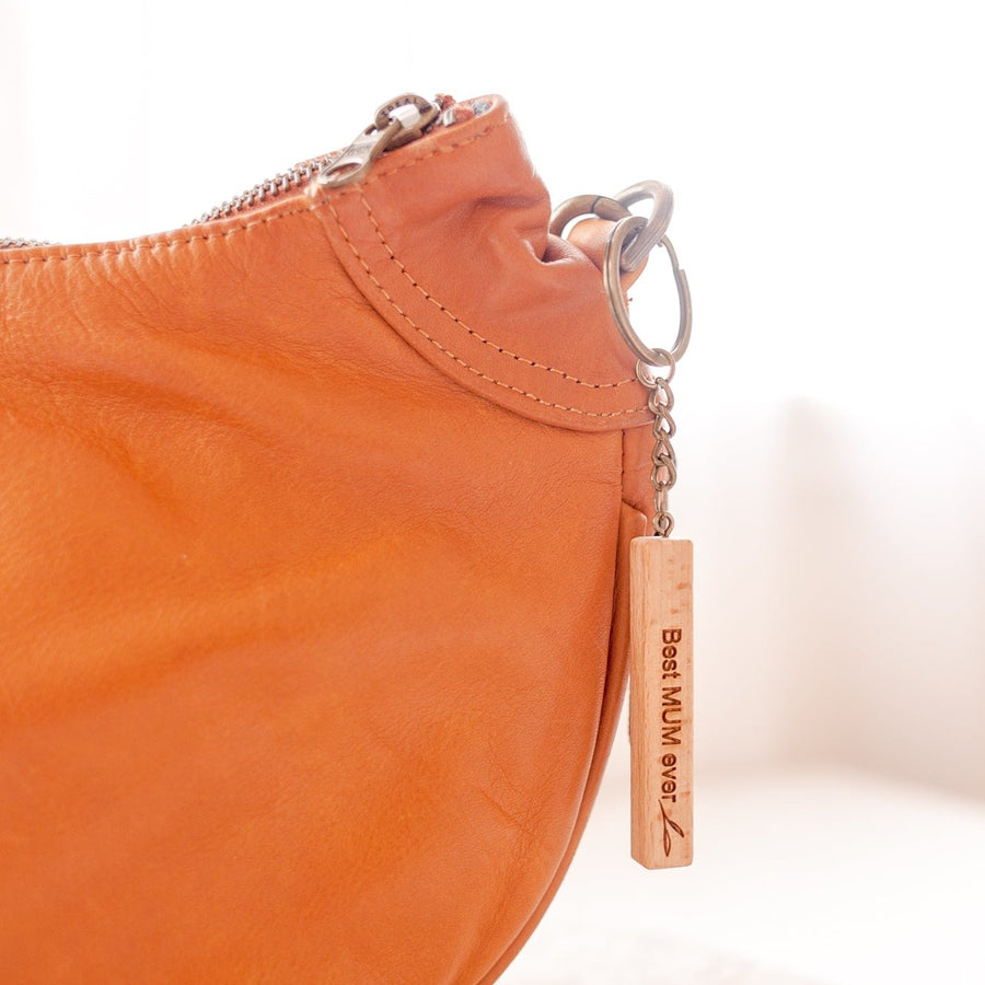 Closeup of Hello Fern light wooden Mother's Day keyring hanging from brown leather bag.