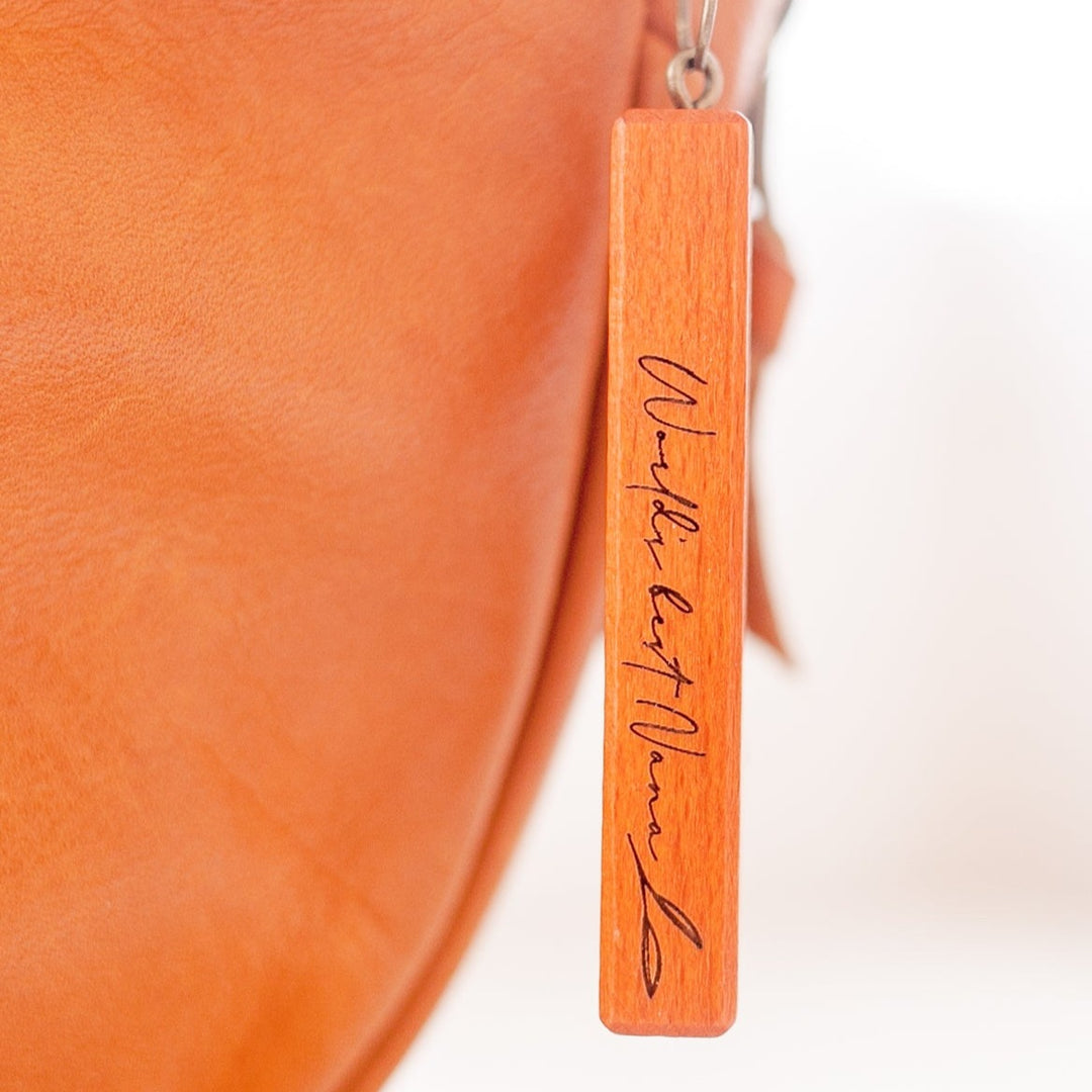 Closeup of Hello Fern dark wooden Mother's Day keyring hanging from brown leather bag.