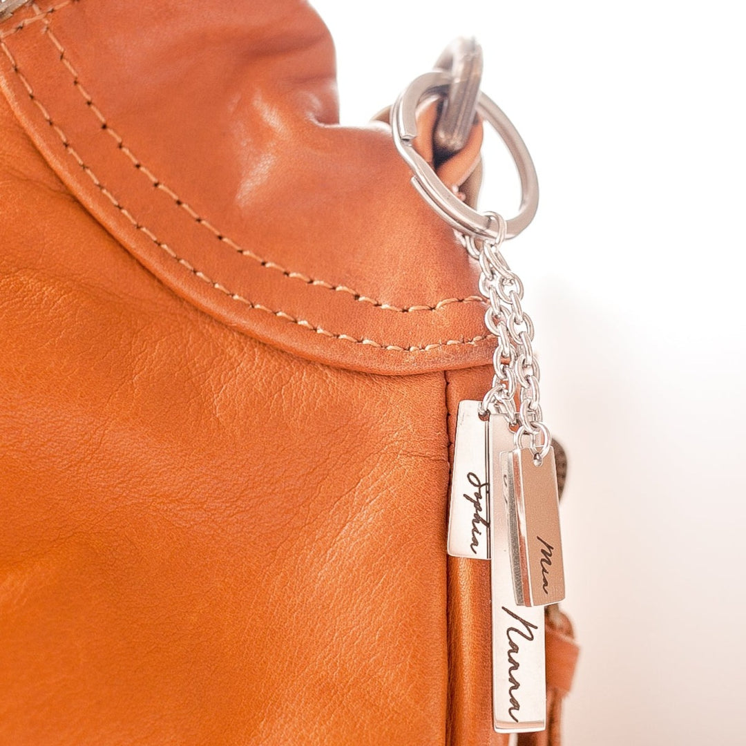 Closeup of Hello Fern personalised silver Mother's Day keyring shown hanging from a brown leather hand bag.